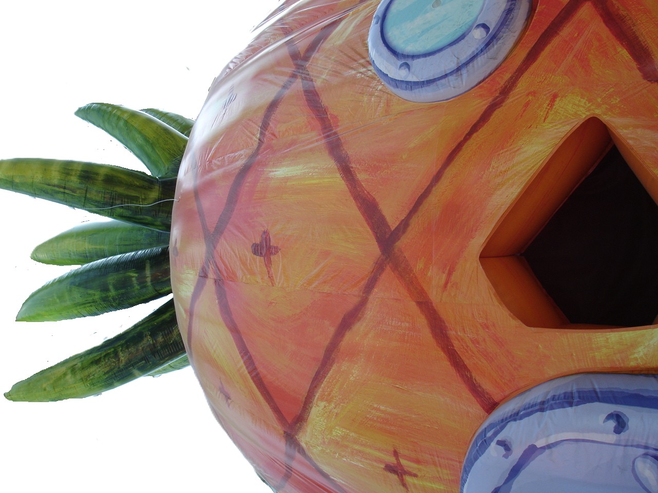 Detailed close-up view of SpongeBob's pineapple house showing the textured diamond pattern exterior with round windows and a wooden door surrounded by pink coral formations